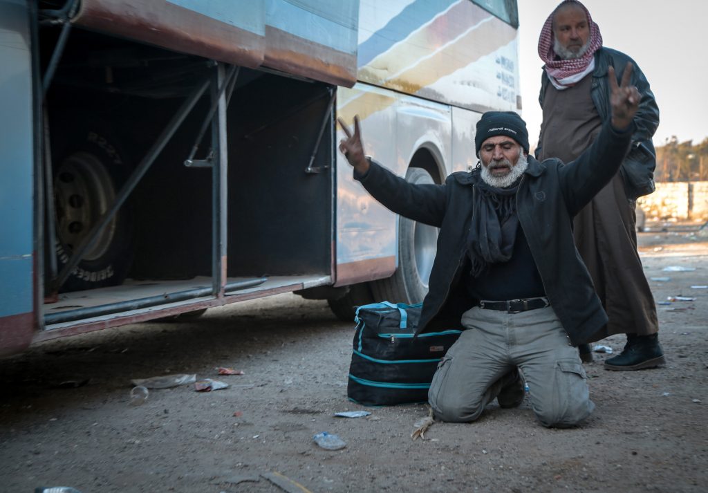 A man drops to the ground with a peace sign after being evacuated from Aleppo